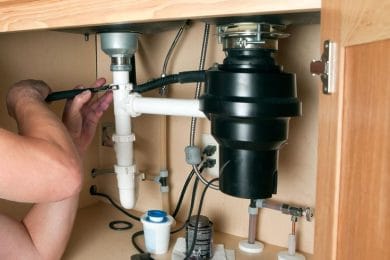 Plumber repairing a garbage disposal beneath a kitchen sink in Union City
