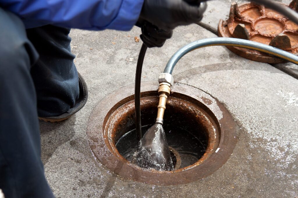 Plumber hydro jetting a sewer line through a manhole in Union City