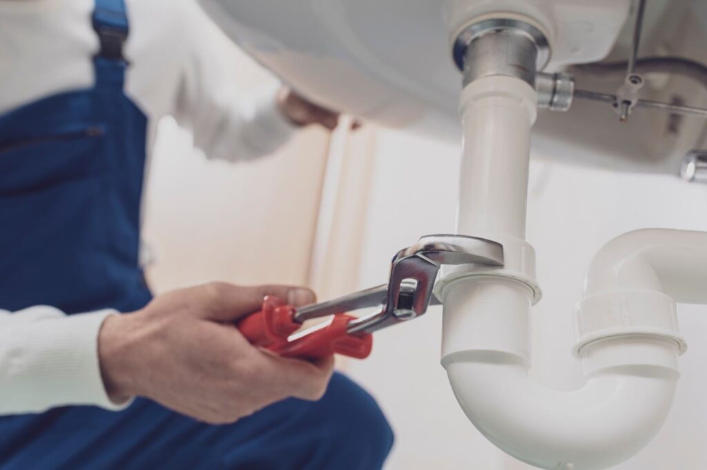 Plumber repairing a white drain pipe beneath a sink in Union City