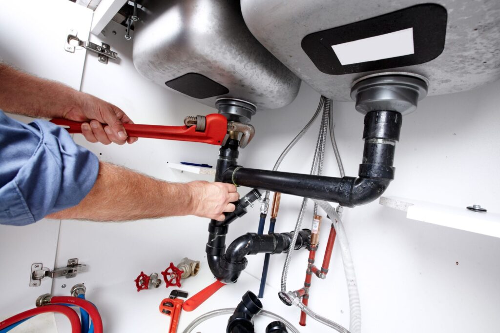 Plumber repairing drain pipes beneath a kitchen sink in Union City